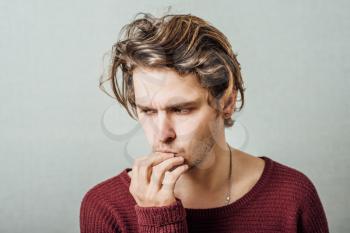 Man thinks upset with his hand to his mouth. On a gray background.