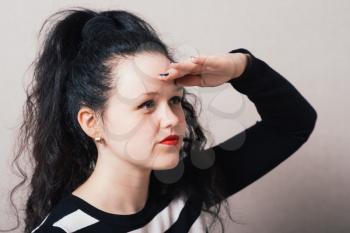 Woman looking into the distance hand near head. Gray background.