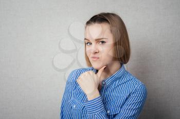 Young adult looking at you while holding chin gray background