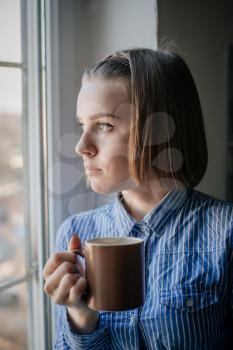 woman drinking coffee in the morning sitting by the window.