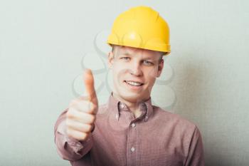 Construction worker in yellow hard hat. Happy male in his 20s. Young man portrait with thumbs up.