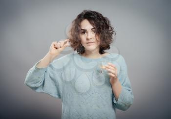 Woman taking pills. Depressed young woman taking a pill while standing against grey background