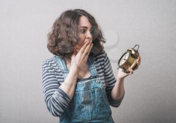 beautiful woman holding an alarm clock in his hands and closed his mouth, dressed in overalls