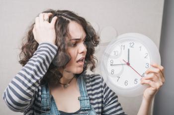 A woman looks at the big clock and holding his head, is late. Gray background