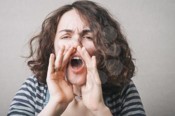 Woman with hands near his mouth, shouting. On a gray background.