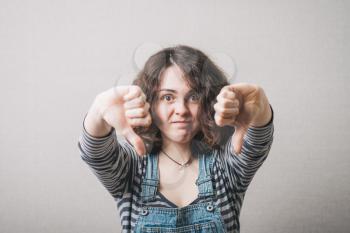 Woman showing two thumbs down. On a gray background.