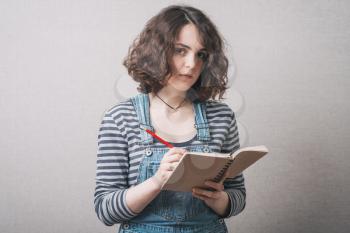 woman writes in a notebook, dressed in overalls