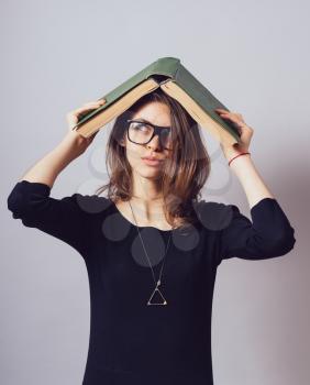 Young beautiful girl in glasses holding big green book playfully on the head