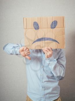 Young man with an unhappy smiley card half covering face