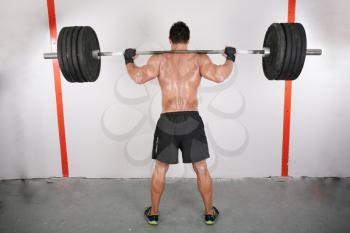 arms and back of a young muscular man working out with a bar