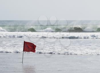 Red warning flag standing against big ocean waves. Bali, Kuta beach.