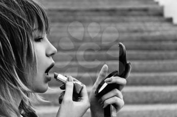Closeup image of beautiful young woman with lipstick and mirror in her hands. Black and white photo