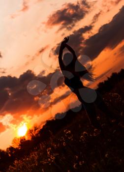 Silhouette of a dancing young girl against the sunset sky