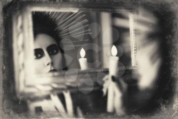 Beautiful goth girl holding candle in hand and looking into the mirror. Grunge texture effect