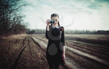Attractive young girl in black dress taking pictures by the classic film camera. Outdoor portrait in the field
