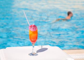 Cocktail glass with umbrella and straw near swimming pool
