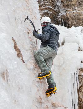 Man with ice axes and crampons climbing on icefall
