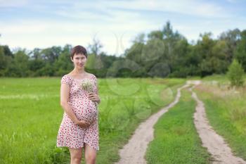 Pregnant woman with chamomile bouquet on the forest road
