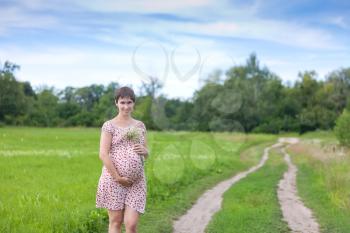 Pregnant woman with chamomile on the forest road
