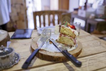 Strawberry cake on wooden table with knife, fork, tablet pc in the cafe
