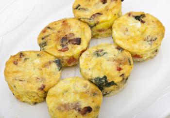 Egg muffins with spinach, bacon, cheese and tomatoes on white plate