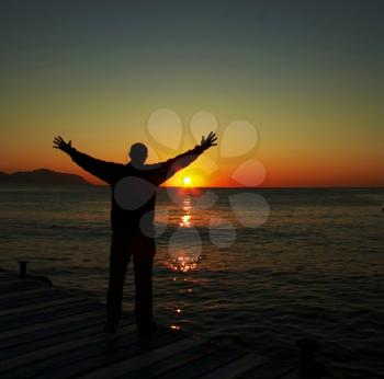 Royalty Free Photo of a Silhouette of a Man Beside a Lake at Sunset
