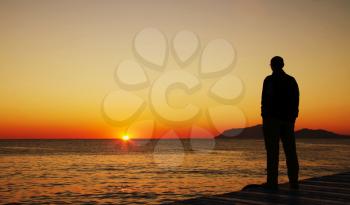 Royalty Free Photo of a Silhouette of a Man Watching a Sunset Over Water