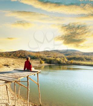 Royalty Free Photo of a Woman Sitting on a Pier at a Lake