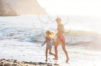 Family on the beach on sunset. Mother and daughter running together.