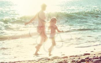 Family on the beach on sunset. Mother and daughter running together.