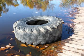 The big old tire from the lorry lies on the bank of beautiful lake in the autumn.