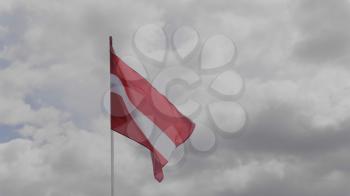 Latvia flag on the flagpole waving in the wind against a blue sky with clouds. Slow motion.