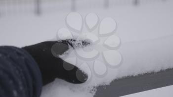 Man in black gloves touches, an icy railing, on a winter street.