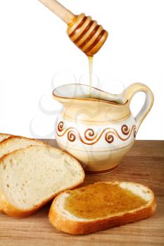 honey in a jug and loaf on board isolated on white background