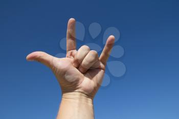 a man hand making the sign of the horns over the sky