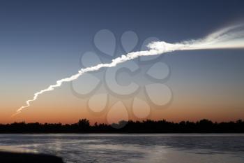 Smoke trail from a rocket at sunset with reflection in water .
