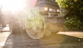 heavy machine rolls a new asphalt road .