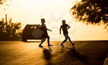 children run across the road at sunset .