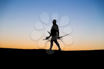 Silhouette of a man with firewood at sunset .
