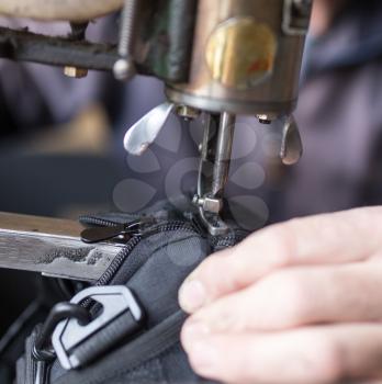 Tailor man sews up a bag in a workshop .