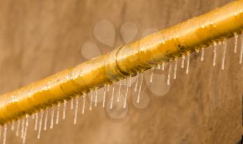 Icicles on a yellow pipe at sunset .