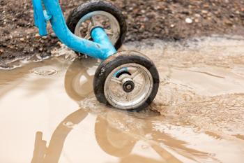 Children's bicycle wheels in a puddle on the road .