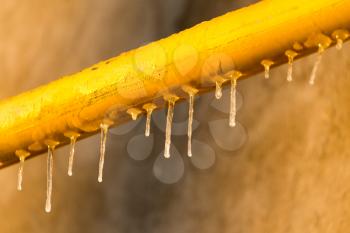Icicles on a yellow pipe at sunset .