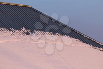 Snow on the roof of the house at sunset .