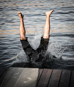 A man dives from shore to lake .