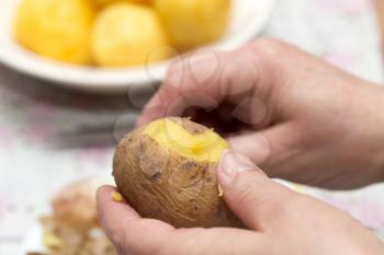 Woman cleaning boiled potatoes with her hands .