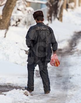 Homeless man is walking on the road in winter .