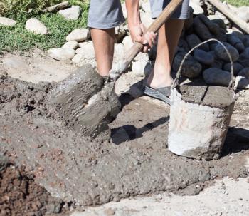 Worker mixes concrete with a shovel at the construction site