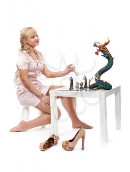 Beautiful blonde girl playing chess with a decorative dragon. Isolate on white.