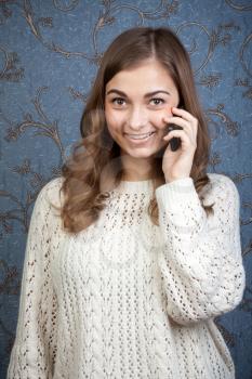 Young beautiful woman with a mobile phone against a background of vintage wallpaper